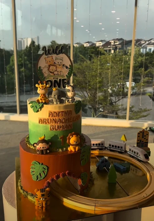 Two-tier wild one themed birthday cake with animal figures and a toy train track